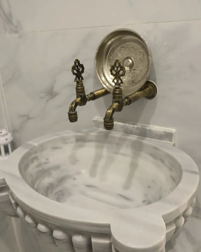 Vasque de hammam en marbre blanc sculpté sous deux robinets en laiton ancien et un bol martelé