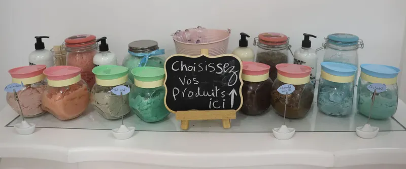 Le bar à gommages du hammam : bocaux pastel étiquetés et petit tableau « Choisissez vos produits ici »