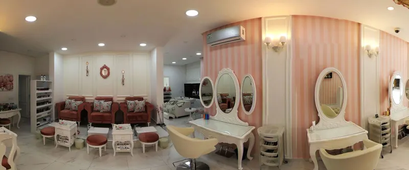 Vue panoramique du salon : fauteuils de pédicure en velours rose, coiffeuses aux miroirs ovales, murs rayés