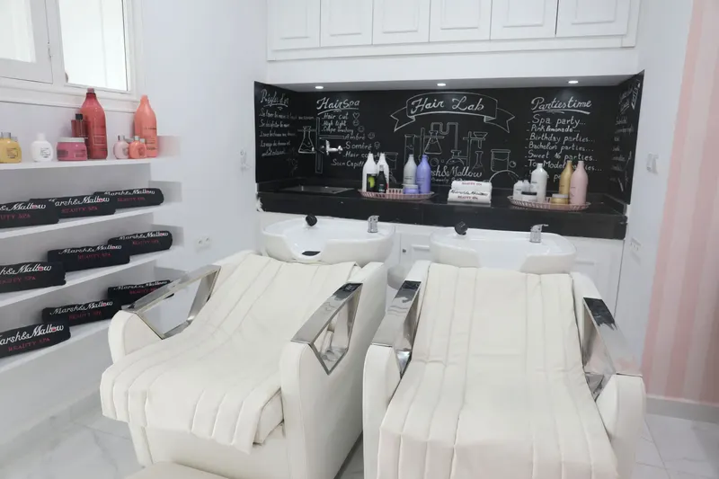 Le Hair Lab : deux fauteuils de lavage blancs sous un tableau noir dessiné à la craie, serviettes noires brodées Marsh&Mallow