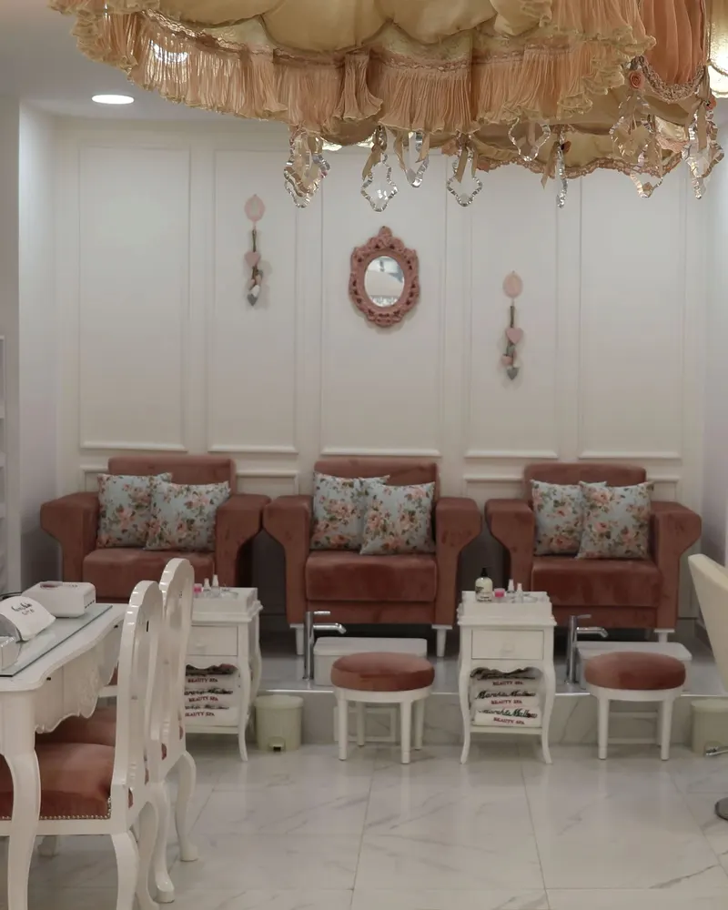 Les trois fauteuils de pédicure en velours rose côte à côte, sous le lustre à pampilles et le petit miroir rose