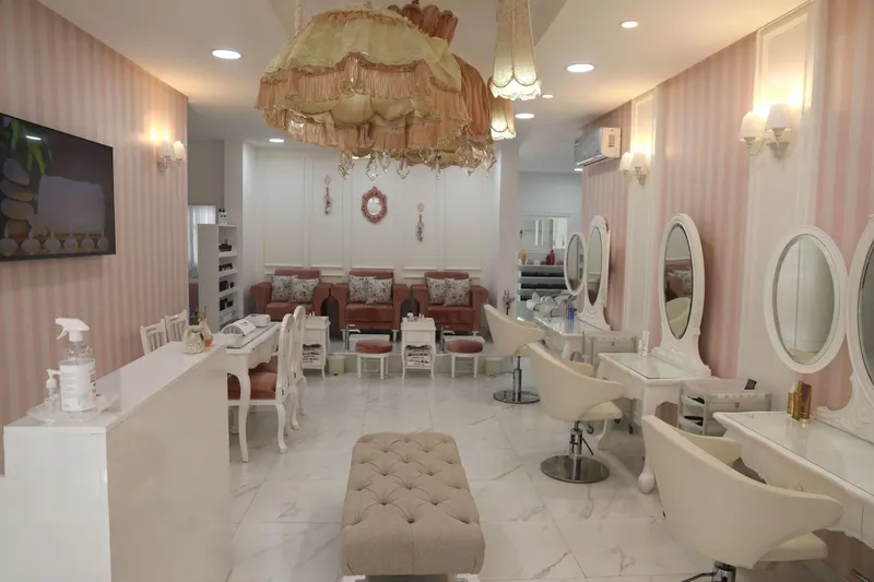 Le salon Marsh&Mallow : murs rayés rose et blanc, lustre d’abat-jour à franges, coiffeuses blanches aux miroirs ovales, fauteuils de pédicure en velours