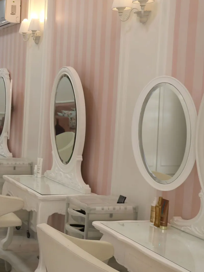 Les coiffeuses blanches aux miroirs ovales, sur le mur rayé rose du salon