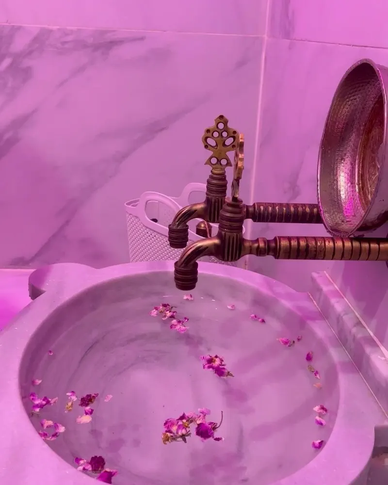 La vasque du hammam remplie de pétales, sous la lumière rose